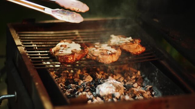 Cooking pork chops on hot charcoal grill with smoke rising during outdoor barbecue party