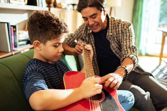Man teaching boy to play guitar at home