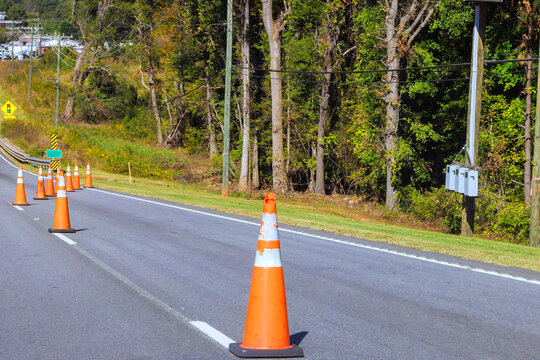 Orange traffic cones guide vehicles along road beside utility poles during road maintenance.