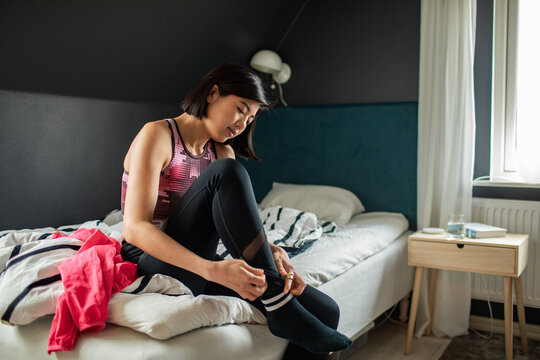 Woman in sportswear putting on socks in bedroom