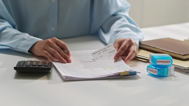 Professional business person reviewing financial documents at desk with calculator and stacked paper files in modern office setting