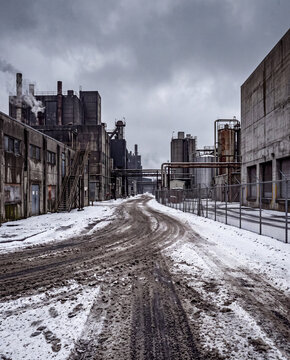 Snow-covered service road between industrial buildings on an overcast winter day