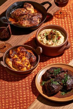 Georgian chicken tabaka and chkmeruli served with braised beef cheeks on a patterned runner, featuring warm golden crusts for a culinary menu