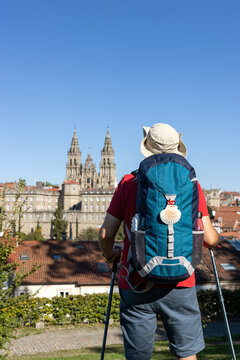 A pilgrim with a backpack with a scallop shell motif gazes from a distance at the Cathedral of Santiago de Compostela after completing the Camino de Santiago.