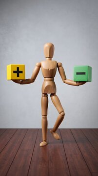Wooden mannequin balancing plus and minus blocks in hands.