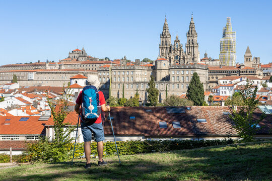 Rear view of a pilgrim contemplating from above Santiago de Compostela and its majestic cathedral on sunny day