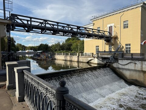 Historic riverside waterworks with industrial footbridge, weir, yellow building, and calm reflections