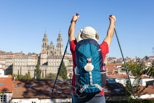 A pilgrim on the Camino de Santiago raises his hiking poles in front of the Cathedral of Santiago, celebrating the end of his journey.