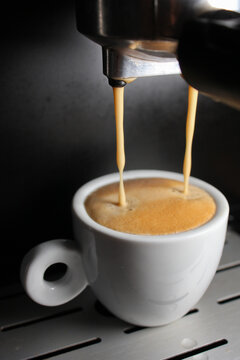 Close up of an espresso coffee machine pouring two streams of fresh coffee into a white ceramic cup with thick crema