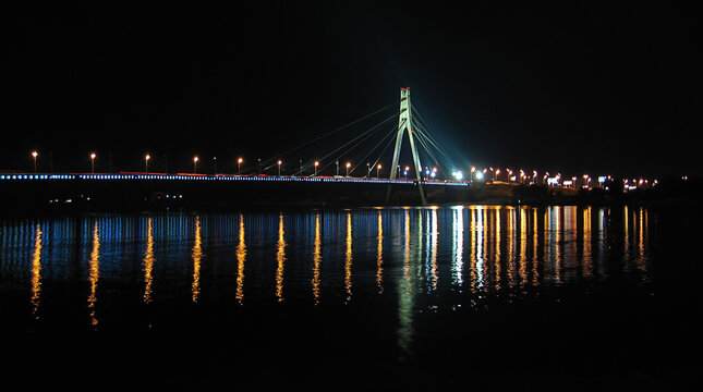 Night view of the Northern bridge with illuminated blue lights and reflection in Dnieper river in Kyiv Ukraine