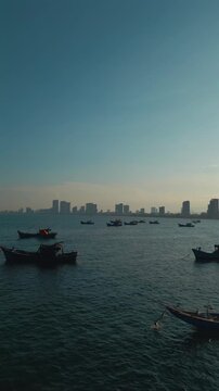 fishing boats anchored in sea bay with Danang city skyline on horizon, high angle coastal seascape view in Vietnam, aerial drone view, vertical video 4k