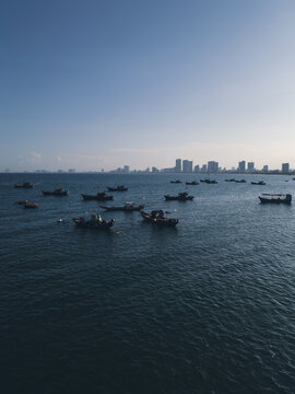 fishing boats anchored in sea bay with Danang city skyline on horizon, high angle coastal seascape view in Vietnam, aerial drone view