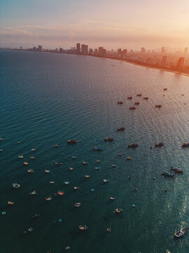 fishing boats anchored in sea bay with Danang city skyline on horizon, high angle coastal seascape view in Vietnam, aerial drone view