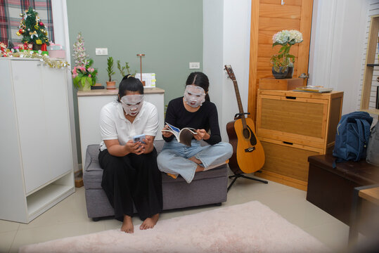 Facial mask woman read book while friend uses smartphone for skincare routine, during beauty treatment activity together in cozy home living room for indoor leisure lifestyle concept