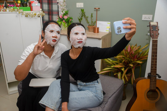 Facial mask woman takes selfie with friend using smartphone for skincare routine, during beauty treatment activity together in cozy home living room for indoor leisure lifestyle concept