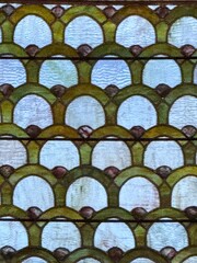 Close up of antique leaded stained glass with a repeating scalloped arch pattern in green, frosted white, and amber, creating an ornate abstract texture background © Frances