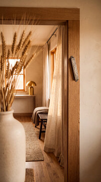 Hammered metal mezuzah affixed to a wooden doorpost in a warm, sunlit modern rustic home interior with dried wheat in the foreground