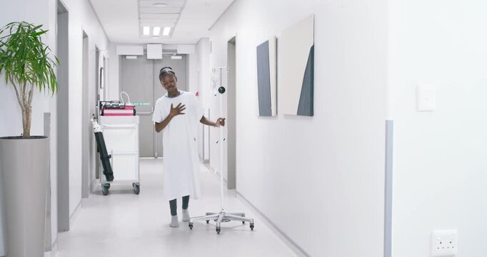 African American woman steadying on IV pole, wearing gown, walking toward double doors in hospital