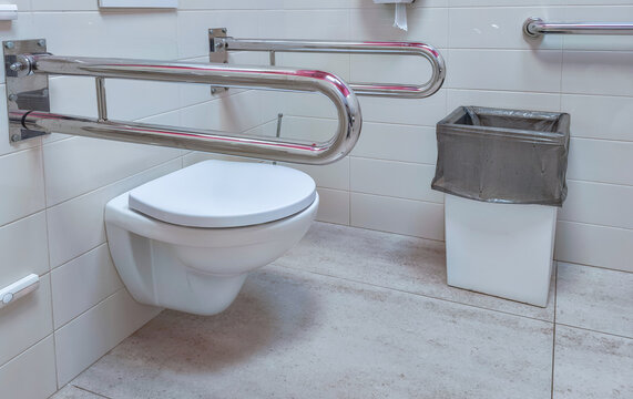 Accessible toilet with wall mounted grab bars in tiled bathroom. Universal design for mobility and independent living. Public restroom accessibility and disability inclusion