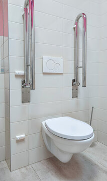 Wall-mounted toilet with grab bars in accessible tiled bathroom. Accessible restroom design for mobility support and independent use. Universal design and disability access