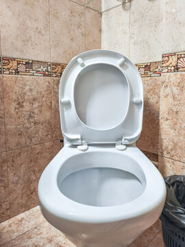 Open toilet in tiled bathroom with raised seat and lid. Bathroom sanitation and personal hygiene. Indoor plumbing fixture for restroom maintenance and cleaning