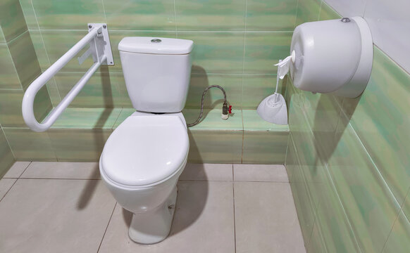 Accessible toilet with grab rail in tiled bathroom. Public restroom accessibility and inclusive design. Mobility support and independent living. Sanitation and hygiene facilities