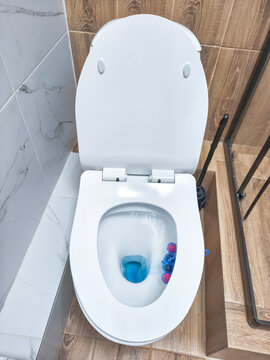 Open toilet bowl with blue cleaner in tiled bathroom. Toilet cleaning and household sanitation. Bathroom hygiene and plumbing maintenance. Domestic cleaning supplies and restroom care