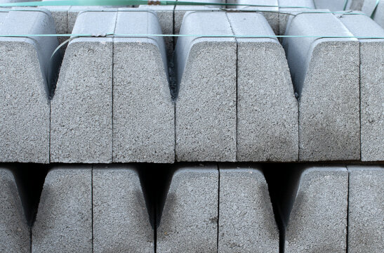 Pallets of stacked, prefabricated concrete kerbstones bound with plastic straps, ready for urban road and pavement construction, featuring a rough grey cement texture.