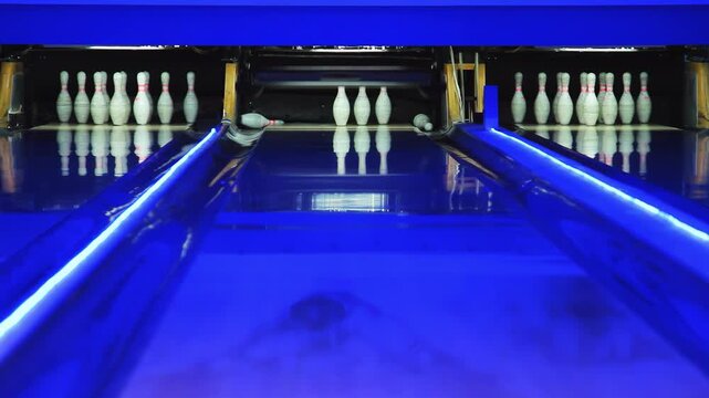 Ball rolling lane knocks down bowling pins. Pinsetter machine colorful lights.