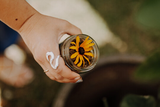 Hand holding a glass jar with a yellow flower and soil