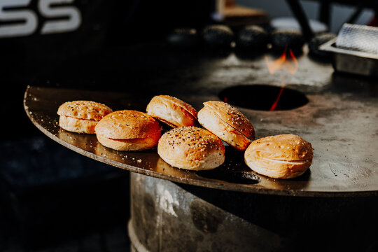 Sesame burger buns toasting on a round grill plate