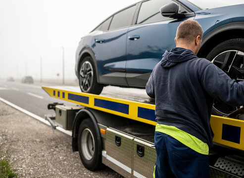 Roadside assistance worker securing a modern electric car on a flatbed recovery truck