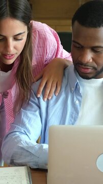 Young multiracial university students looking at a laptop screen together, discussing academic coursework and collaborating on project while sitting at study desk indoors