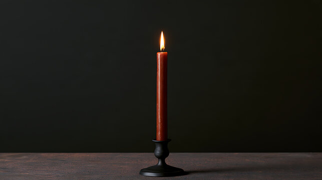 A single lit brown taper candle standing in a vintage black metal holder on dark background, creating a cozy and warm atmosphere at home
