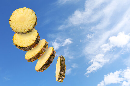 Pineapple slices in air against blue sky with clouds