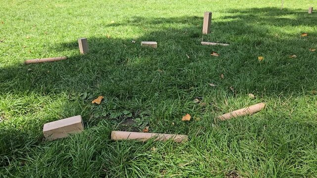 A direct baton hit sends a kubb block flying in the shade of a park tree. Power and accuracy in a classic Scandinavian throwing game for sport and hobby themes.