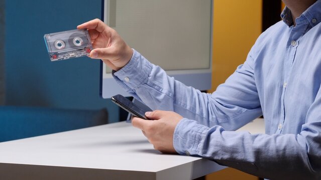 Person holding a cassette tape in one hand and a smartphone in the other, illustrating the shift from analog music formats to digital technology and changing listening habits