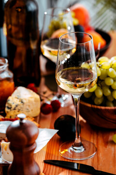 Chablis white wine glass on wooden dining table beside grapes and cheese - gourmet food pairing concept for friendly lunch. Elegant wine tasting layout for dinner party.