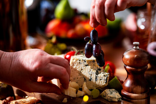 Wine lunch - hands picking dark grapes from cutting board with blue cheese, gourmet food sharing, hospitality event concept, festive autumn dining table arrangement with wine snacks.