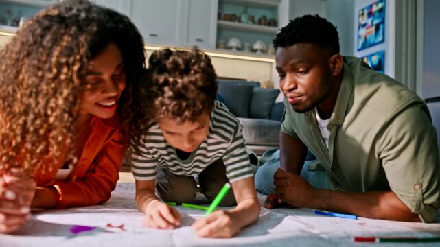 Happy multiethnic family lying floor drawing markers. Boy coloring parents home.