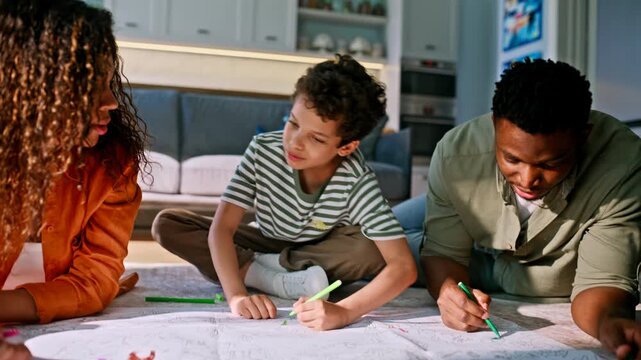 Parents son coloring paper living room floor. Creative multiethnic family time.