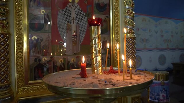 01.01..26. Yuzhno-Sakhalinsk. Russia. Church candles are lit in a candlestick filled with sand. The interior of an Orthodox church with an icon in a gilded frame, thin wax candles, a religious prayer