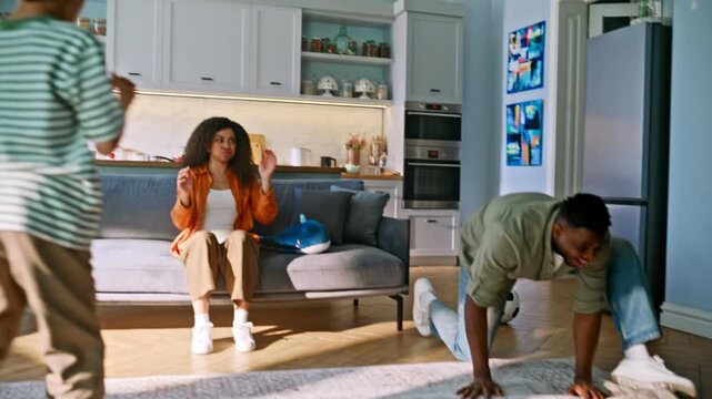 Cheerful son dancing father living room. Parents celebrating soccer goal home.