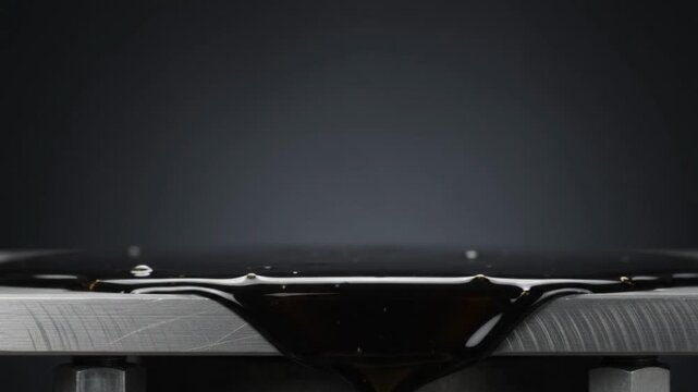 Brushed Stainless Steel Industrial Edge at Bottom with Thin Film of Viscous Crude Oil Gliding Beneath Clean Charcoal Copy Space