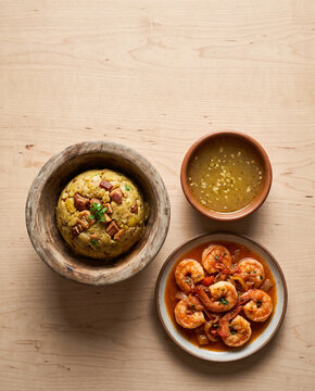 Puerto Rican mofongo in a wooden pilon with garlic broth and shrimp in tomato sauce, top view with copy space, vertical