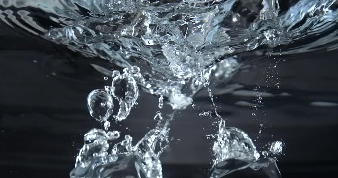 Ice cubes dropping into water creating splash closeup slow motion