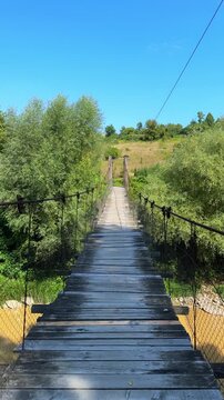 A wooden suspension bridge over a river in a rural landscape