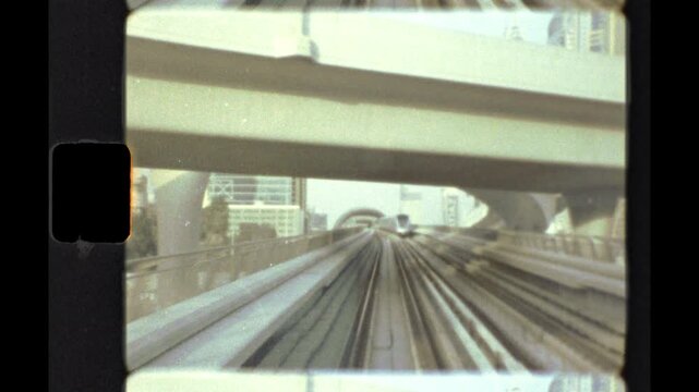 Color Super 8 film shows a Dubai metro train passing on an elevated track beside skyscrapers, seen from the front of another train