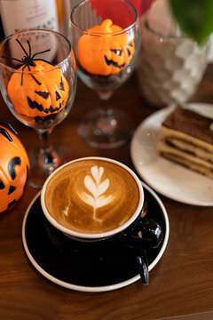 Hot coffee latte with latte art milk foam in cup mug with decor in a coffee and tiramisu cake decorated with cute edible eyeball  a theme of halloween on wood desk Halloween holiday background.