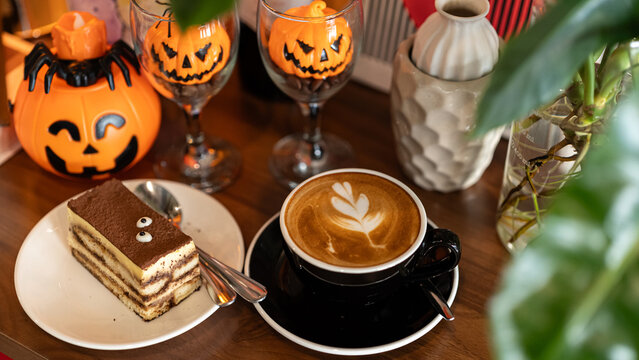 Hot coffee latte with latte art milk foam in cup mug with decor in a coffee and tiramisu cake decorated with cute edible eyeball  a theme of halloween on wood desk Halloween holiday background.